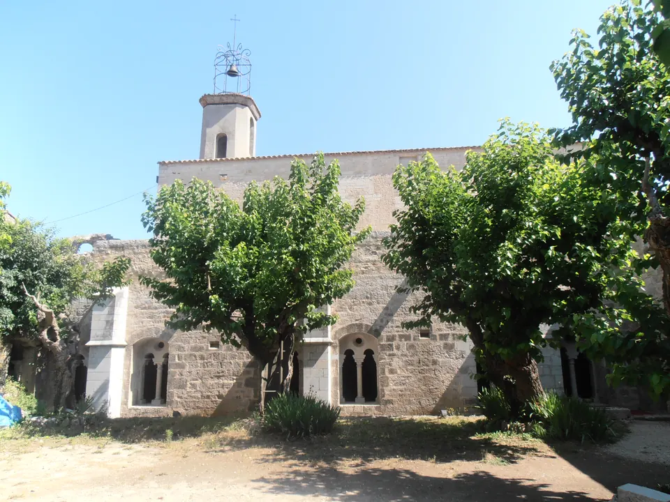 Bâtiments en pierre et clocher de l’abbaye de La Celle, derrière les arbres.